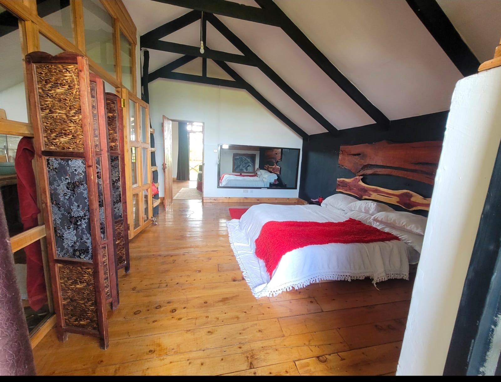 Rustic cabin bedroom with wood floors, exposed beams, and a red throw blanket.
